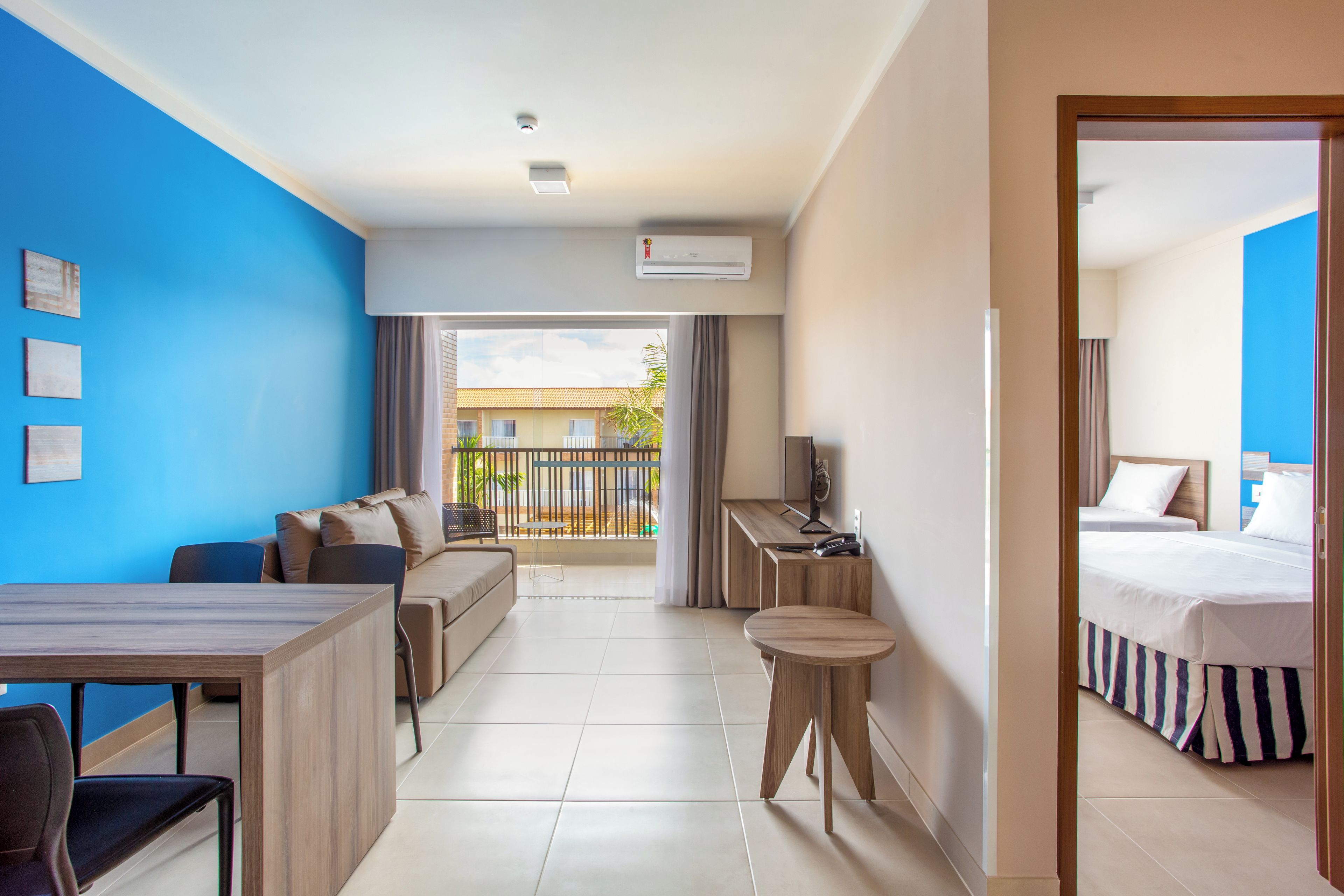 Habitación de hotel con cama, escritorio, silla, sofá y mesa de comedor. Tiene un balcón con vistas al exterior.