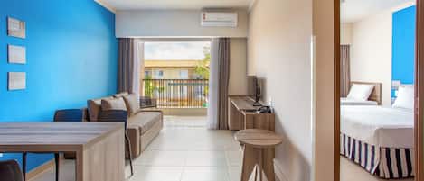 Habitación de hotel con cama, escritorio, silla, sofá y mesa de comedor. Tiene un balcón con vistas al exterior.