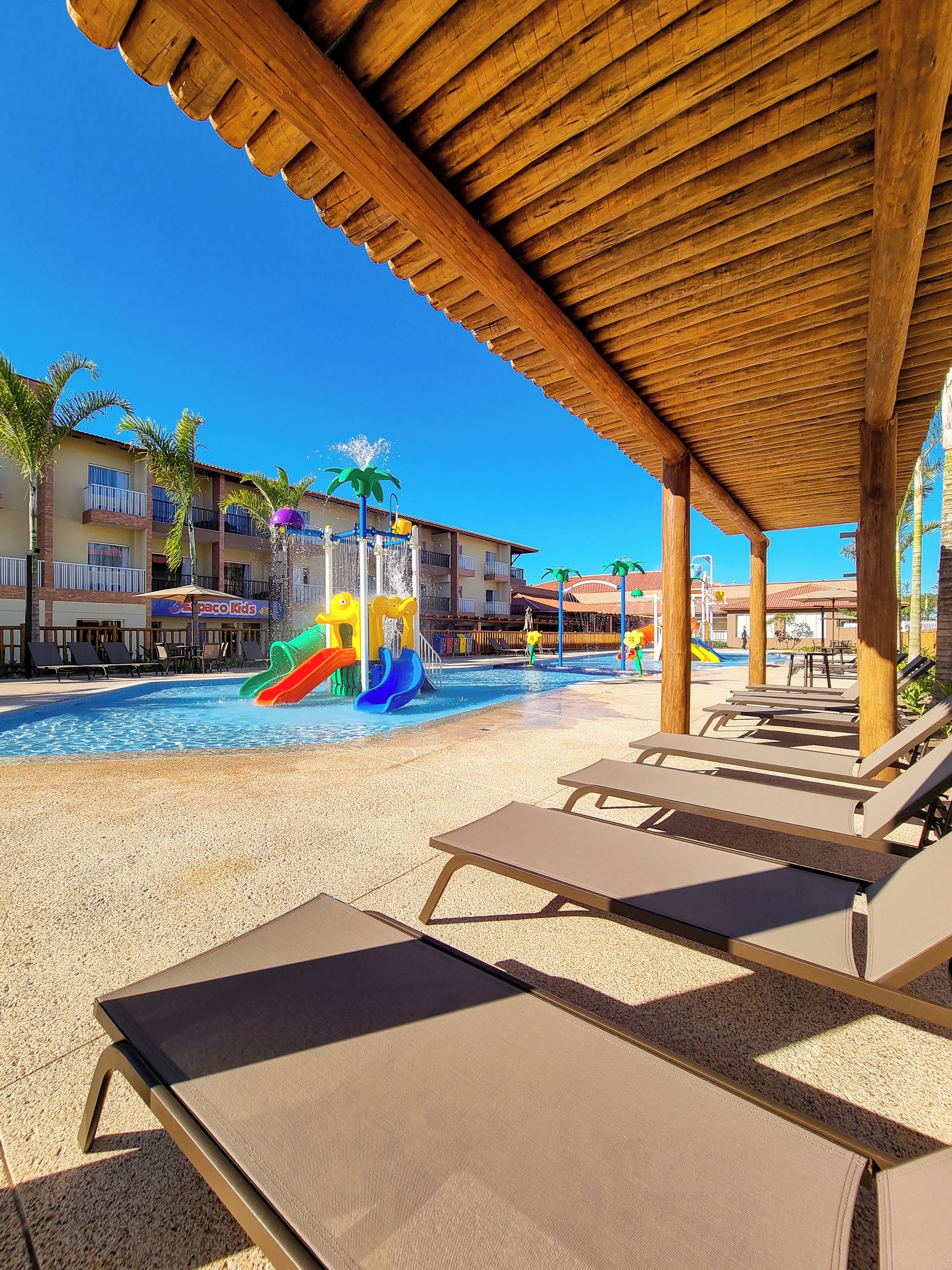 A pool area with lounge chairs, a water slide, and a building with balconies.