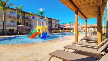 A pool area with lounge chairs, a water slide, and a building with balconies.
