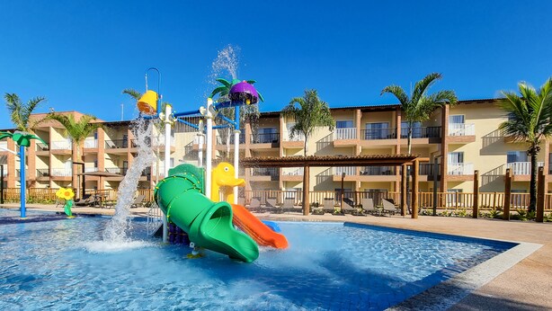 A water park with slides and a pool area, surrounded by a multi-story building with balconies. - Ondas Praia Resort by WAM Experience (Porto Seguro)