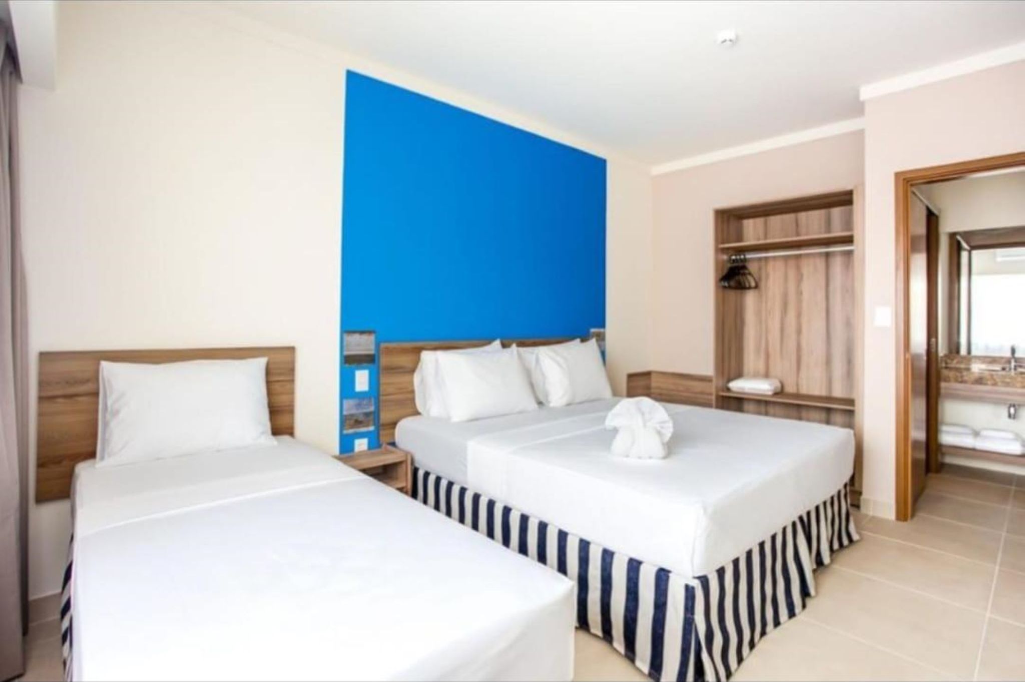 Une chambre d’hôtel avec deux lits, un mur d’accent bleu, une tête de lit en bois, une table de chevet, un miroir et une salle de bain avec un lavabo et un porte-serviettes.