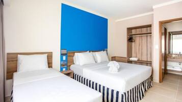 Une chambre d’hôtel avec deux lits, un mur d’accent bleu, une tête de lit en bois, une table de chevet, un miroir et une salle de bain avec un lavabo et un porte-serviettes.