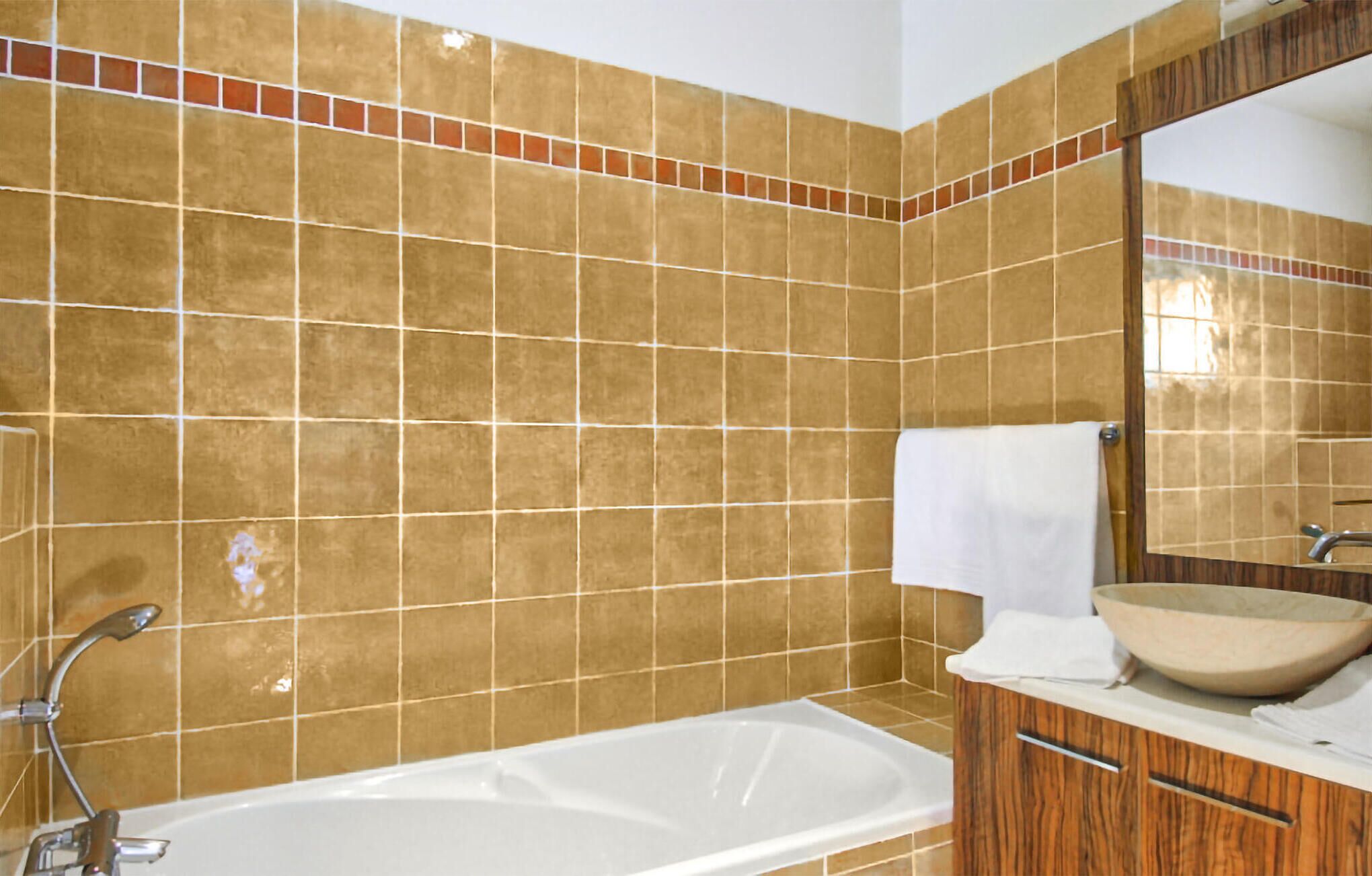 Ein Badezimmer mit einer Badewanne, einem Holzanfang, einem Spiegel und braunen Fliesenwänden.