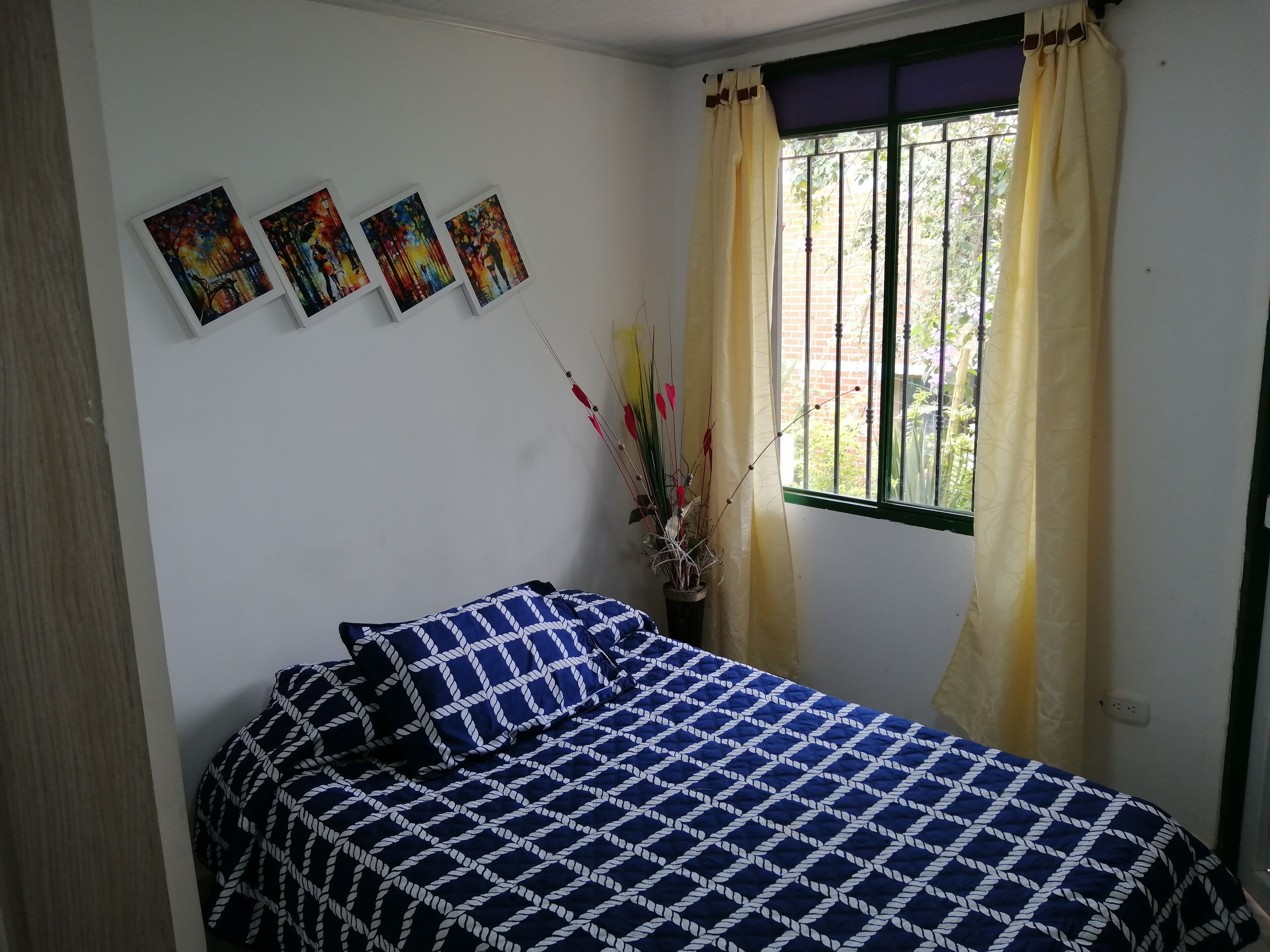 Quarto com uma cama, uma janela com cortinas e três quadros na parede.