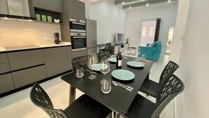 Una cocina moderna con electrodomésticos integrados y un comedor con una mesa negra dispuesta para cuatro.