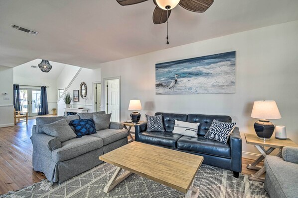 A spacious living room with a large sofa, a coffee table, and a fireplace. There is a painting on the wall and a ceiling fan above. - Pool Access & Steps to Beach: Coastal Getaway! (Gulf Shores)