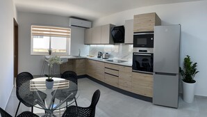 Cozinha moderna com forno embutido, micro-ondas e frigorífico. Há uma mesa de jantar com cadeiras e um vaso de plantas.