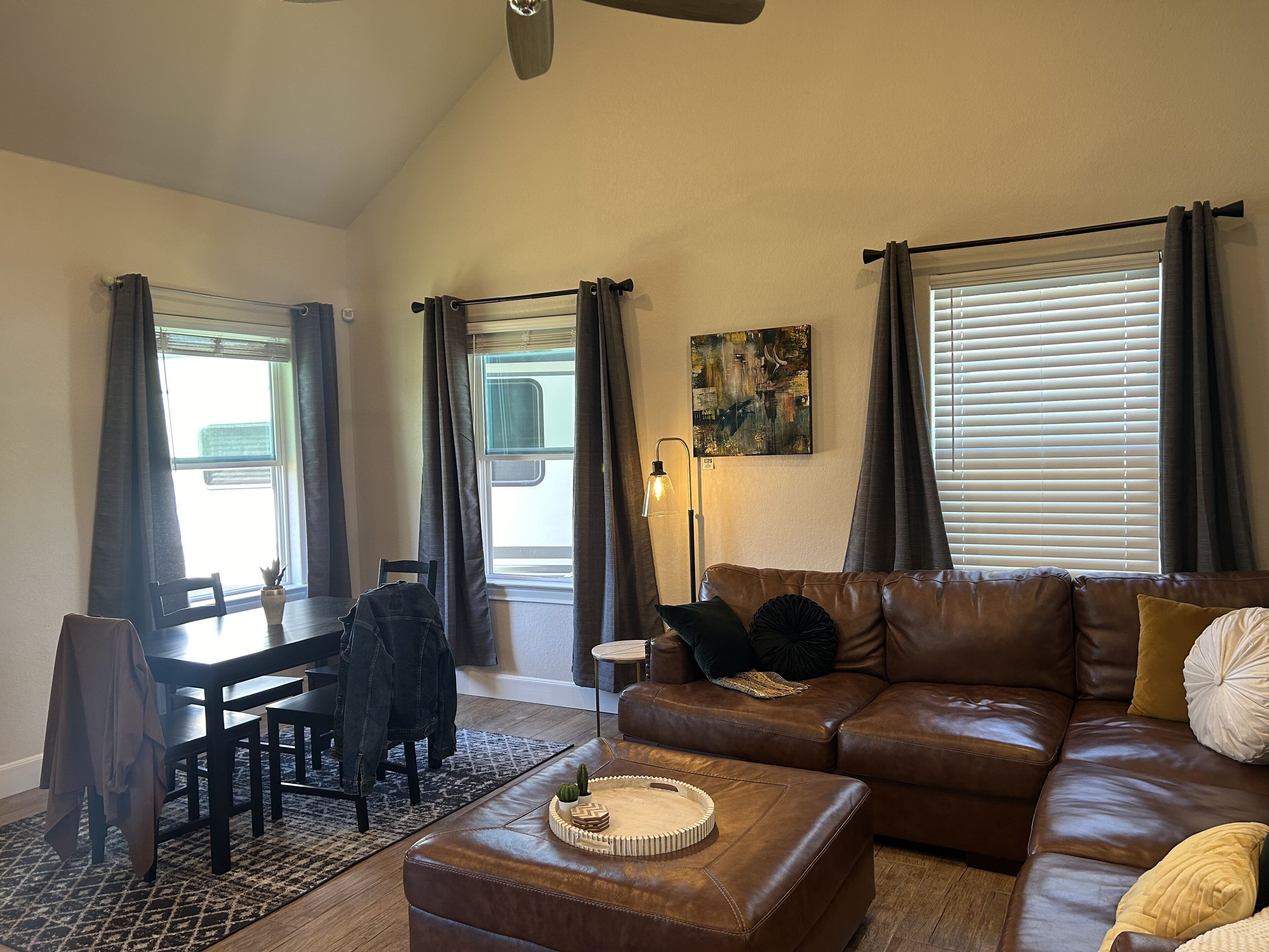 A living room with a brown leather sofa, a dining table with chairs, and a coffee table with decorative items.