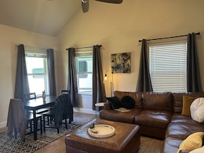 A living room with a brown leather sofa, a dining table with chairs, and a coffee table with decorative items.