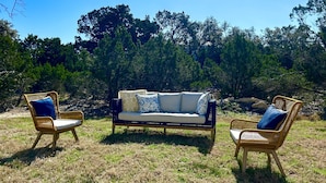 A wicker sofa with patterned cushions in a grassy outdoor area with trees in the background. - Fun New Lake House! (Canyon Lake)