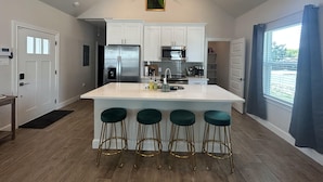 A modern kitchen with white cabinets, stainless steel appliances, and a central island with bar stools. - Fun New Lake House! (Canyon Lake)