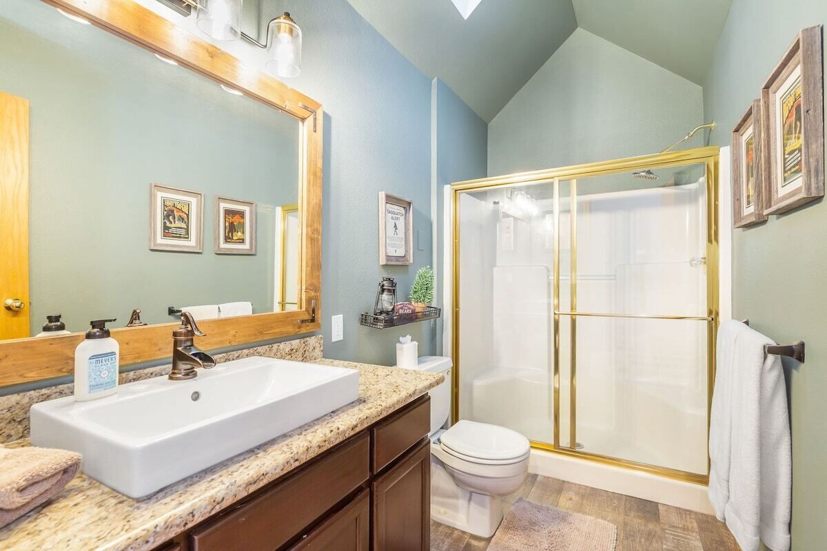 Un baño con un lavamanos grande, un espejo, un inodoro y una ducha con mampara de vidrio.