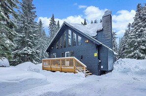 A cabin with a wooden deck, surrounded by snow-covered trees. - Close to Ski + Snowboard | Games | Hiking Trails (Snoqualmie Pass)