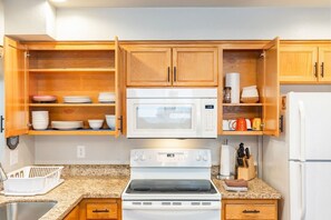 A compact kitchen with wooden cabinets, a microwave, stove, and a refrigerator.