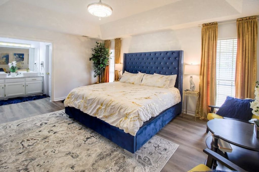 A bedroom with a large bed, a bedside table, a lamp, and a view of the bathroom.