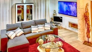 En stue med en grå sofa, et glasbord, et fladskærms-tv og en statue.