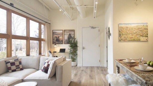 A spacious living room with a sofa, a coffee table, and a dining area with a table and chairs. There is a door leading to another room and a window providing natural light. - Chic View Loft at Historic Plaza - Spacious 470 Sq Ft (Santa Fe)
