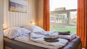 Un dormitorio con cama, almohadas, un cuadro, una ventana con cortinas y vista a un patio de recreo.