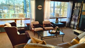 A cozy living room with a fireplace, comfortable seating, and large windows offering a view of trees. - Amazing Views! 2 BR 8-person Condo Lake Tomahawk/Minocqua Chain, Dock included (Lake Tomahawk)