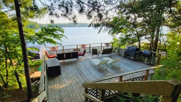 A wooden deck with outdoor seating and a view of a lake. - Amazing Views! 2 BR 8-person Condo Lake Tomahawk/Minocqua Chain, Dock included (Lake Tomahawk)