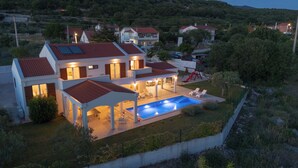 Une maison à deux étages avec une piscine, un espace salon extérieur et un toit recouvert de tuiles rouges.