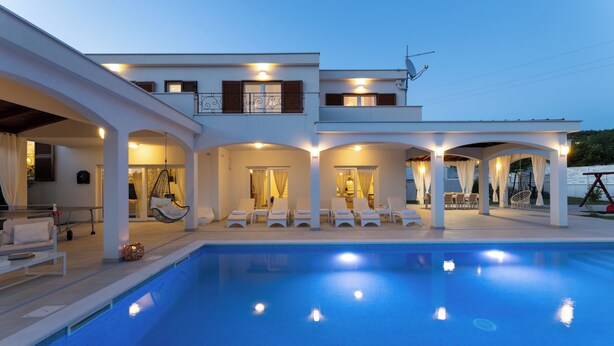 Un bâtiment moderne à deux étages doté d’une piscine, d’un espace extérieur aménagé et d’un patio couvert.