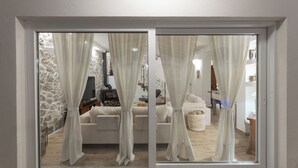 Une pièce avec un mur en pierre, un canapé blanc, un plancher en bois et une porte en verre ornée de rideaux légers.