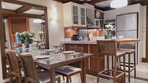 Una cucina moderna con mobili bianchi, un frigorifero in acciaio inossidabile e un'area pranzo con tavolo in vetro e sedie in legno.