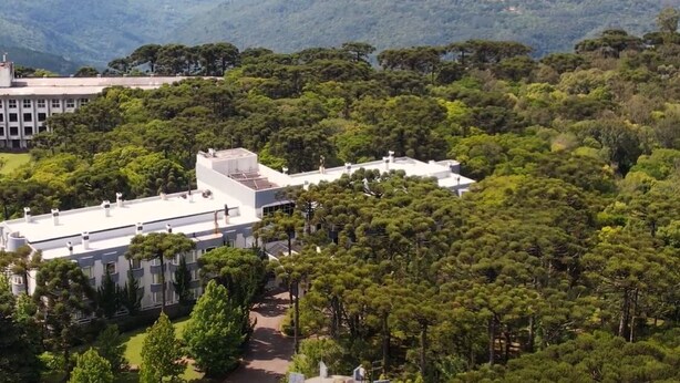 Un edificio moderno con tetto piatto, circondato da vegetazione lussureggiante e colline sullo sfondo.
