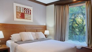 Un letto rifatto con lenzuola e cuscini bianchi, una testiera in legno, un quadro incorniciato sopra e una finestra con tende.