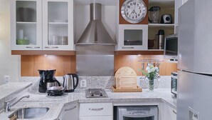Una cucina moderna con mobili bianchi, elettrodomestici in acciaio inossidabile, una macchina per il caffè, un bollitore e una sveglia.