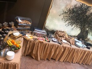 A buffet table with various food items and utensils, a fruit bowl, and a decorative tree mural in the background.