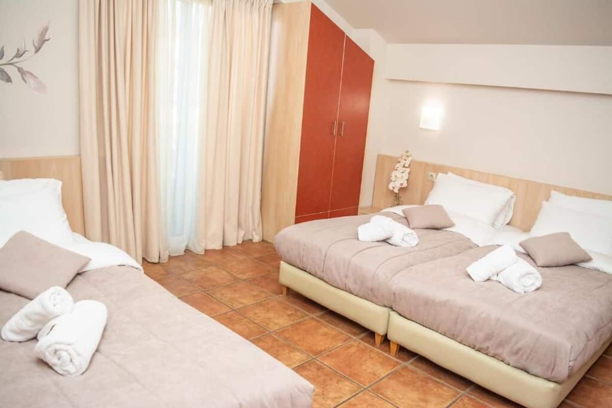 Habitación de hotel con dos camas, cortinas color beige, un armario de madera y una planta en maceta.