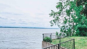 A concrete pathway with a metal railing leading to a grassy area beside a body of water.