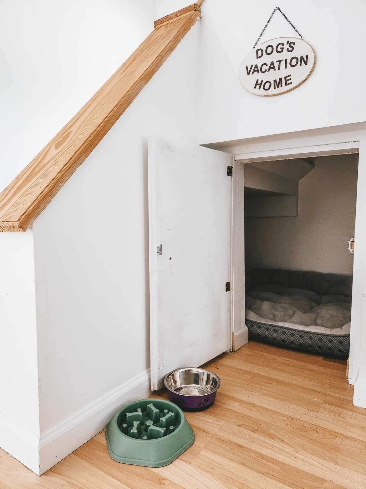 A room with a wooden staircase, a door leading to a dog bed, and a sign reading "DOG'S VACATION HOME".