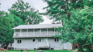A two-story house with a balcony, surrounded by trees and a grassy yard.