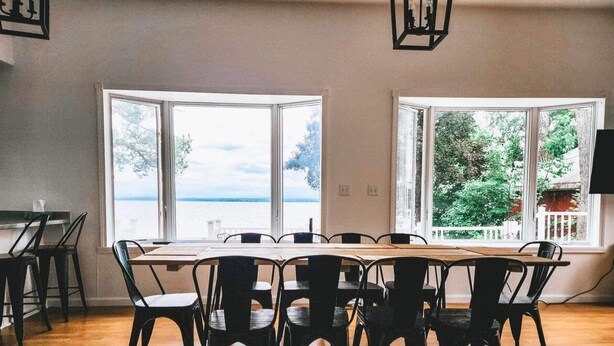 A dining area with a large table and chairs, large windows with a view of the sea, and a wooden floor.