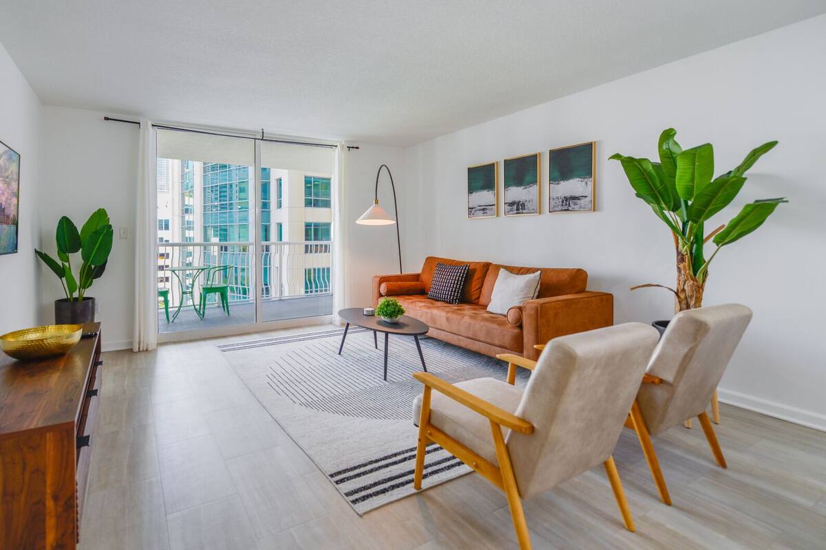 Sala moderna com sofá, cadeiras, mesa de centro e uma janela grande com vista para edifícios.