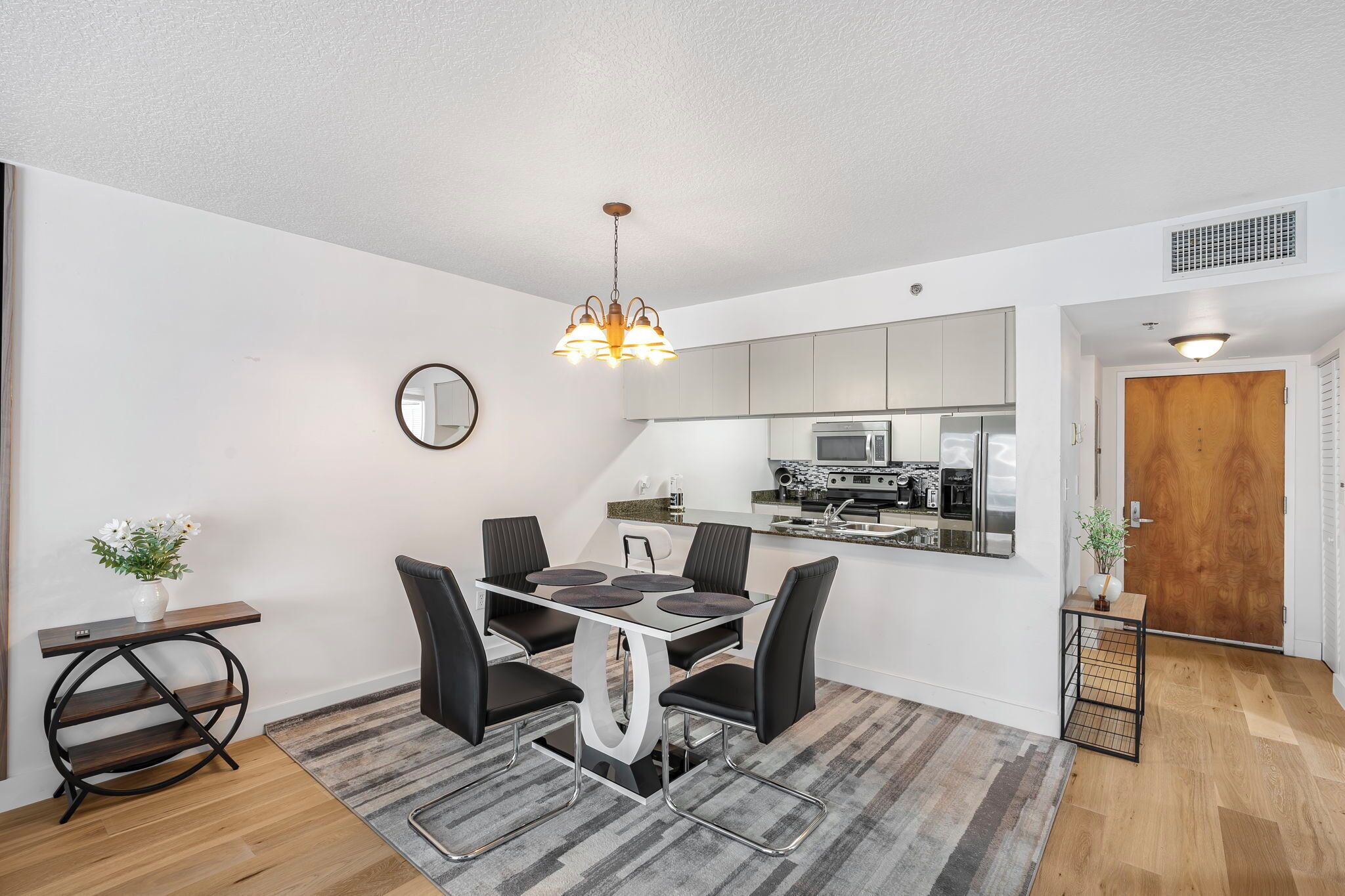 A modern kitchen with a central island, a dining area with a round table and chairs, and a small side table with a vase.