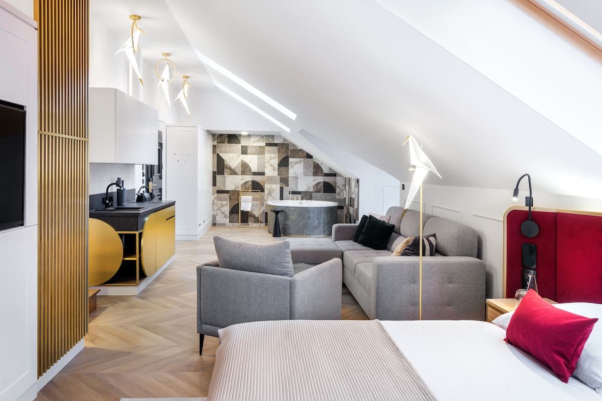 A modern loft bedroom with a built-in kitchen, a large bed, and a seating area with a red accent pillow.