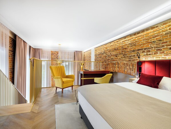 A modern bedroom with a brick wall, a bed, a desk, and a yellow armchair. - Hotel Golden Queen (Kraków)