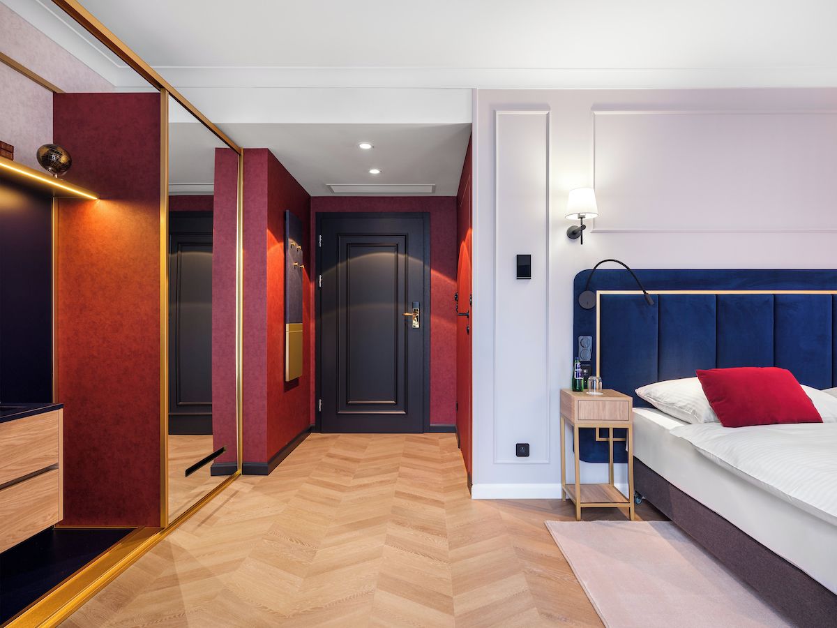 A hotel room with a bed, bedside table, and a mirror.