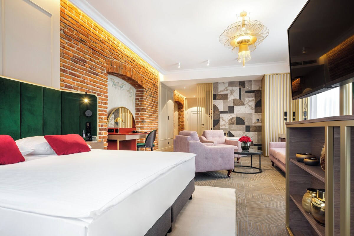 A hotel room with a large bed, a desk, a chair, a sofa, and a television.