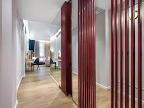 Un couloir d’hôtel avec un plancher en bois, un lit, un bureau et une chaise au fond.