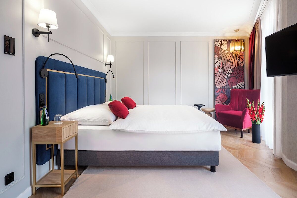 A modern bedroom with a large bed, bedside tables, a TV, and a red chair.