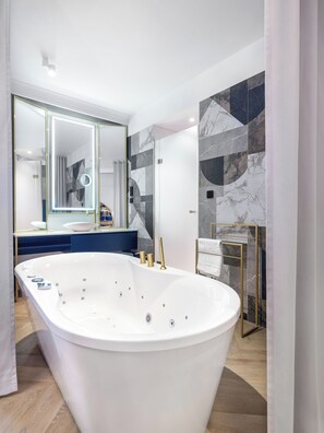 A modern bathroom with a freestanding bathtub, a large mirror, and a marble-tiled wall. - Hotel Golden Queen (Kraków)