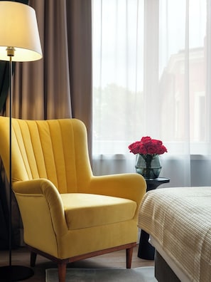Un fauteuil jaune, une table de chevet avec un vase de fleurs rouges et une lampe dans une chambre d’hôtel.
