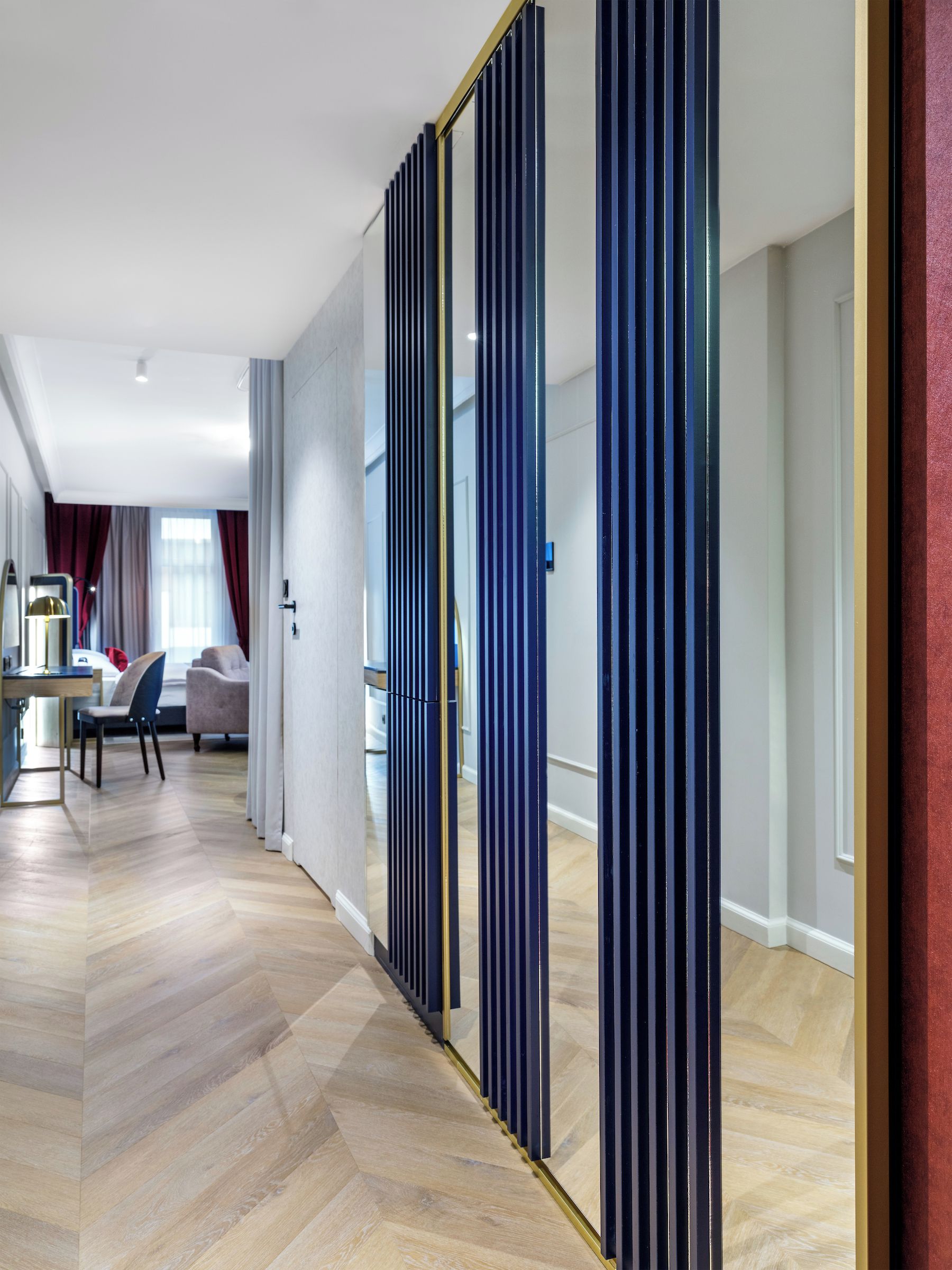 A modern hotel room with a wooden floor, a desk, a chair, and a bed.