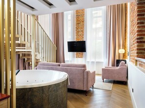 A modern living room with a large bathtub, a staircase, and a brick wall. - Hotel Golden Queen (Kraków)